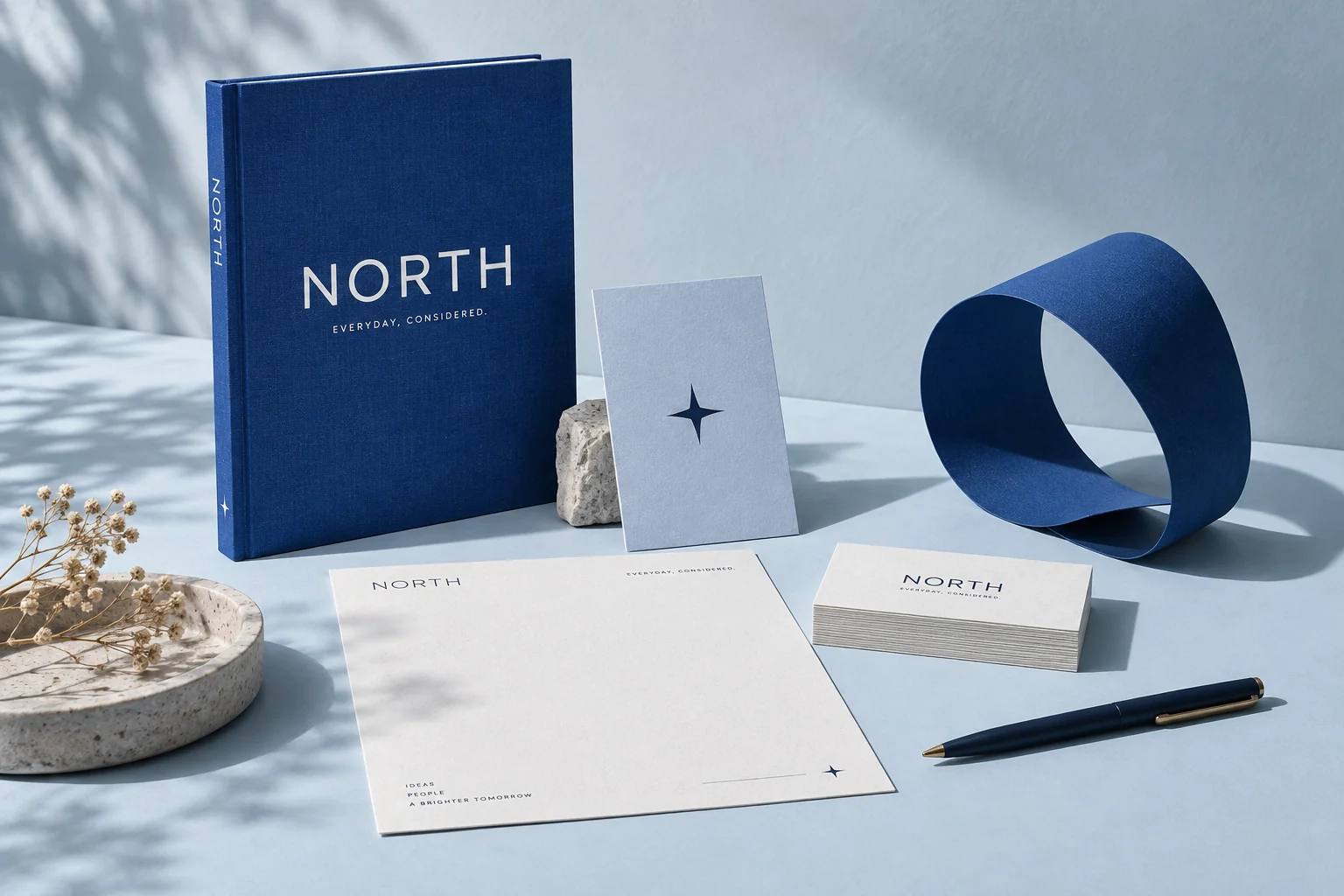 Studio North identity concept with a navy notebook, pale stationery, business cards and a curved blue paper sculpture.